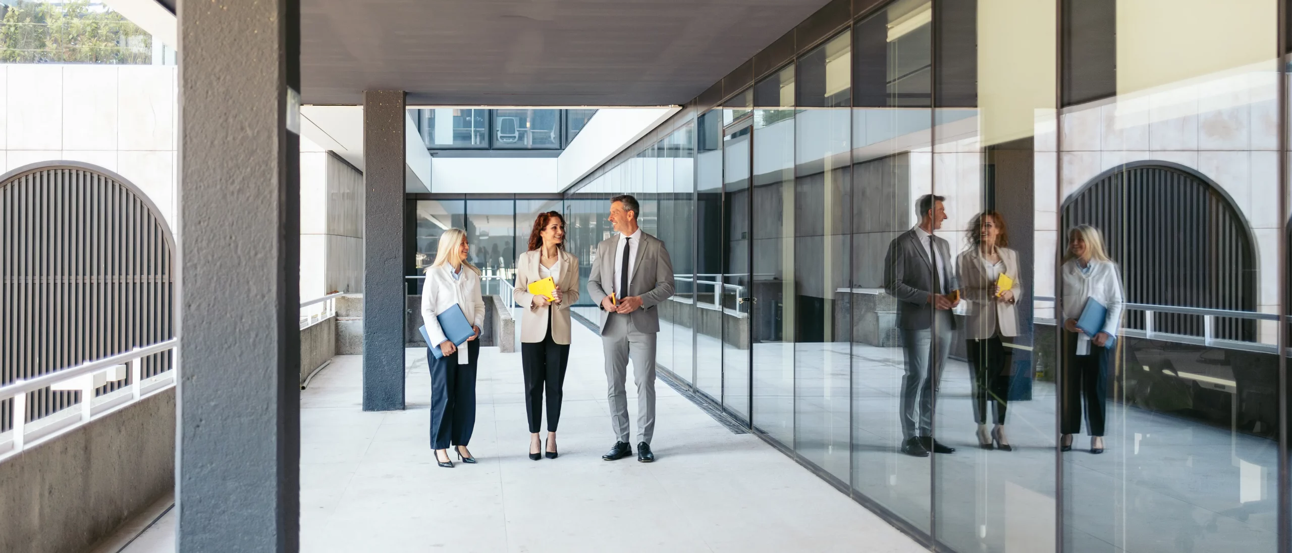 Zwei Frauen und ein Mann laufen an der Glasfront eines Bürgebäudes entlang